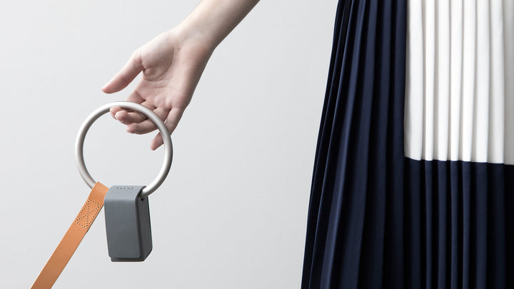 A woman wearing a blue dress hold the Tan Lumi leash with the light grey Toto bag. 